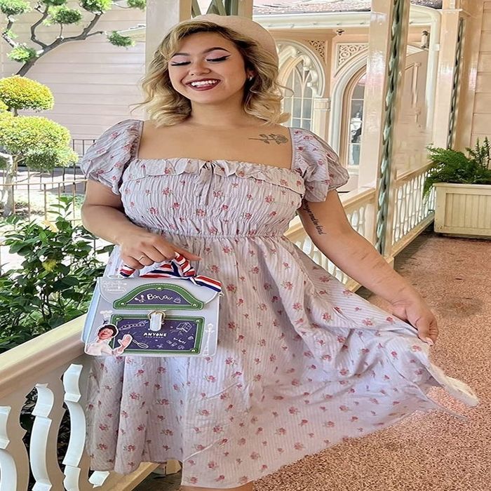 A reviewer is seen in a floral dress, posing on a porch with topiary plants in the background.
