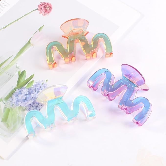 Three iridescent claw clips arranged on a white surface, surrounded by flowers.