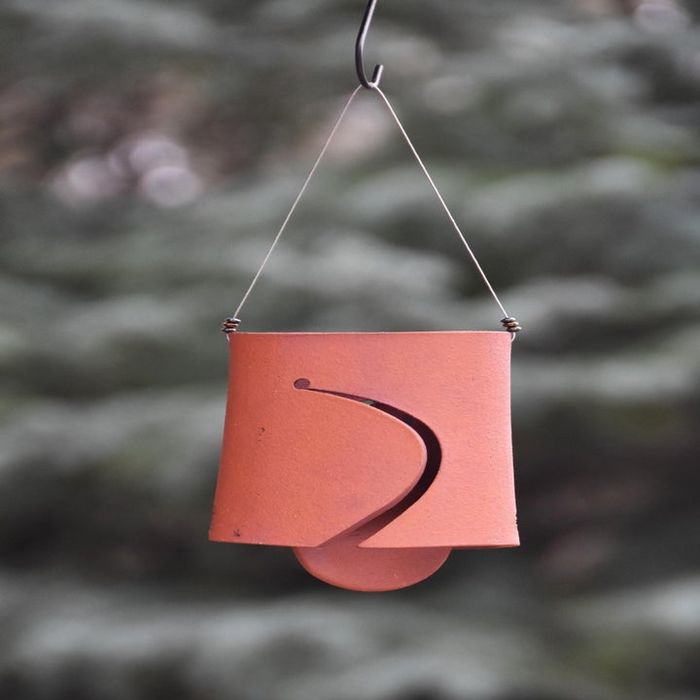 A terracotta wind chime swaying with an intricate cut-out design, set against a soft-focus leafy backdrop