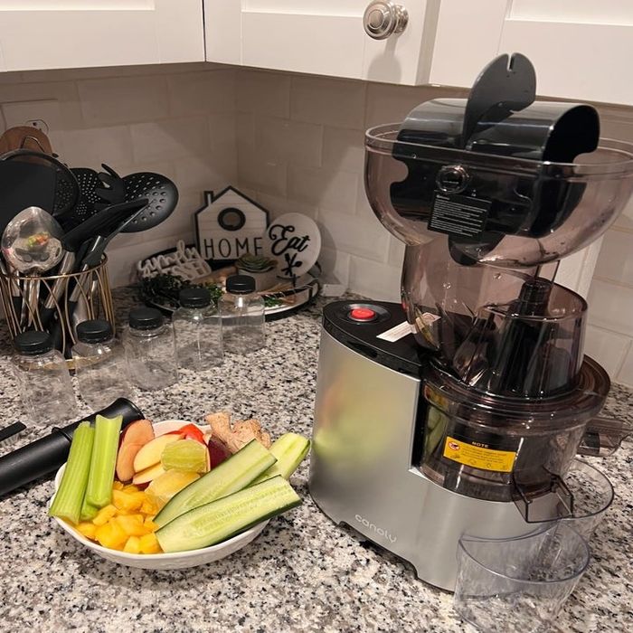 A juicer with a variety of fruits and vegetables ready to be juiced, sitting on a kitchen counter