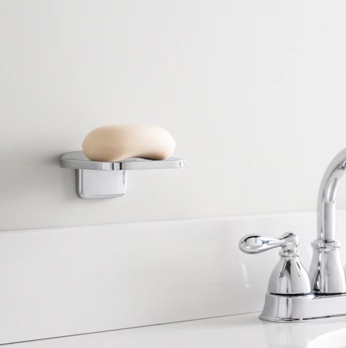 A bar of soap sits on a sleek, wall-mounted soap dish next to a polished chrome faucet in a minimalist bathroom setup.