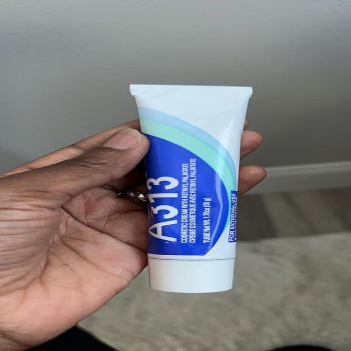 A hand holding a tube of A313 Pommade, a Vitamin A retinoid cream. The label displays dosage instructions in French.