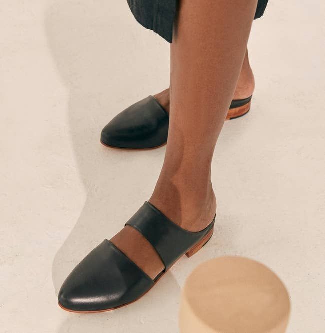 A model showcasing the pointed-toe, open-back flats with a unique cutout detail across the top of the foot.