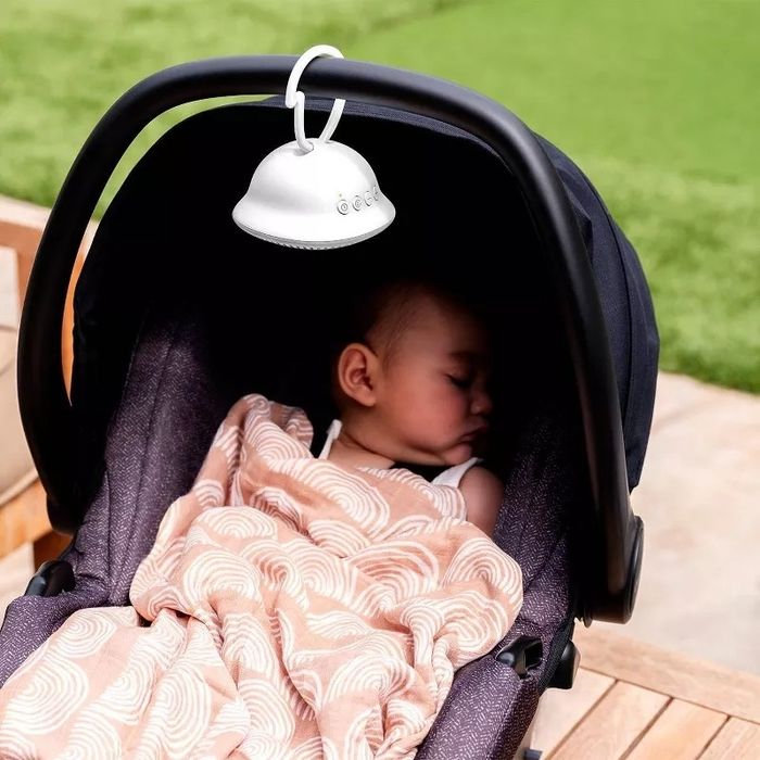 A baby sleeps in a stroller, covered with a patterned blanket, while a clip-on fan is attached to the stroller handle. This image is featured in a Shopping article