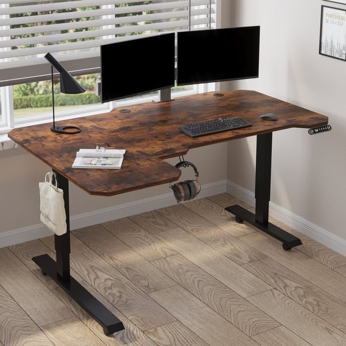 A standing desk setup with dual monitors, a keyboard, a lamp, headphones hanging on the side, and a small bag, perfect for a contemporary home office