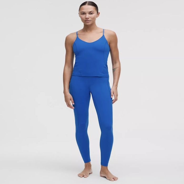 A person dressed in a vibrant blue athletic tank top and leggings set, posing barefoot.