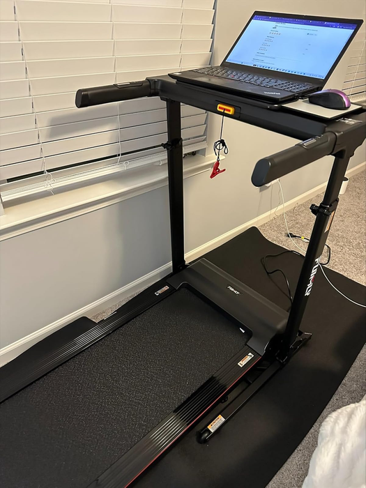 a treadmill paired with a standing desk setup featuring a laptop and mouse, positioned near window blinds