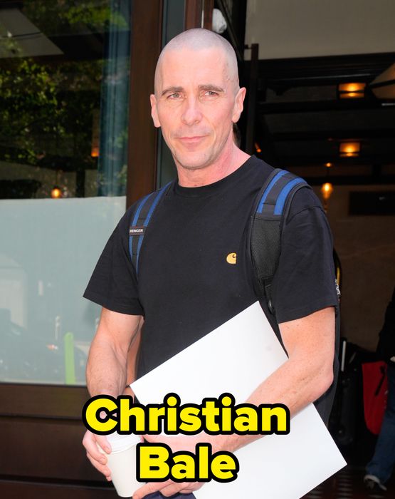 A person wearing a black t-shirt, holding a coffee cup and a white folder, standing in front of a building