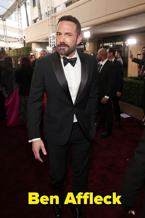 A man in a timeless tuxedo walks the red carpet, with photographers and event-goers surrounding him