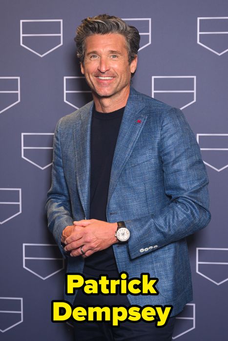 A person in a chic blazer and dark shirt, striking a confident pose with a subtle smile, standing in front of a backdrop with shield-like designs