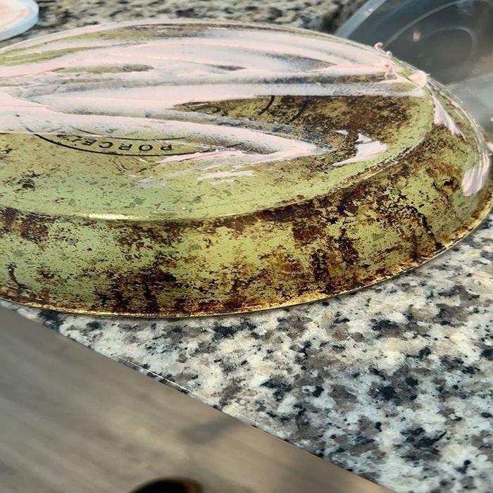 A dirty, upside-down cooking pan resting on a granite countertop, partially covered with plastic wrap