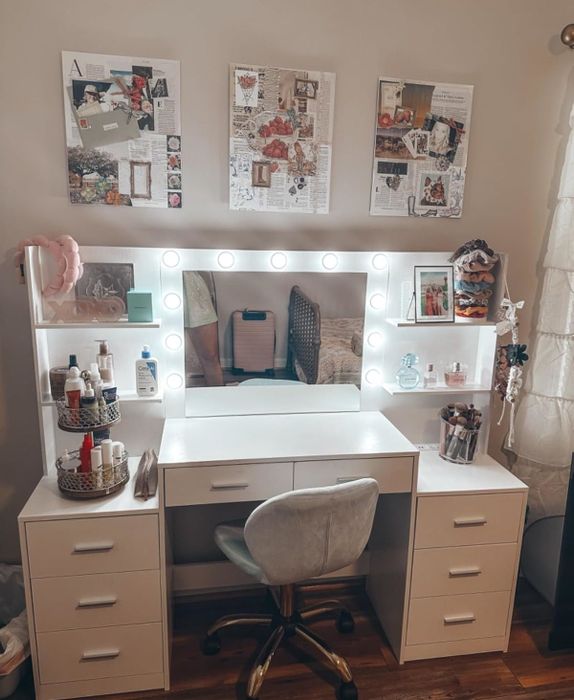 Contemporary vanity setup with a lighted mirror, cosmetics, and decorative pieces arranged on shelves and the desk, complemented by collage art on the wall. Ideal for creating a chic beauty space