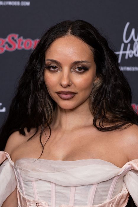 A woman at a red carpet event wearing a stunning off-shoulder gown, with long dark hair and natural makeup
