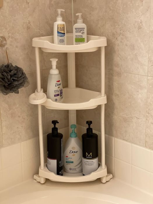 A corner shower caddy with three shelves holding various bottles of lotion, conditioner, and body wash