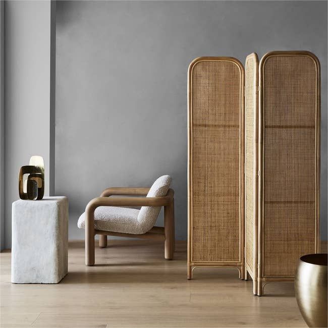 A contemporary living area featuring a wooden room divider, a cozy armchair, a petite stone side table, and carefully curated decorative accents, embodying an earthy and minimalist aesthetic