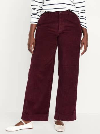 A person styles maroon corduroy wide-leg pants with a striped long-sleeve top and white flats for a casual, stylish look.