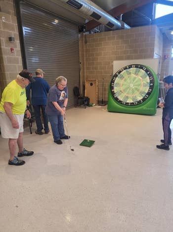 People engage in a golfing activity indoors using a massive inflatable dartboard.