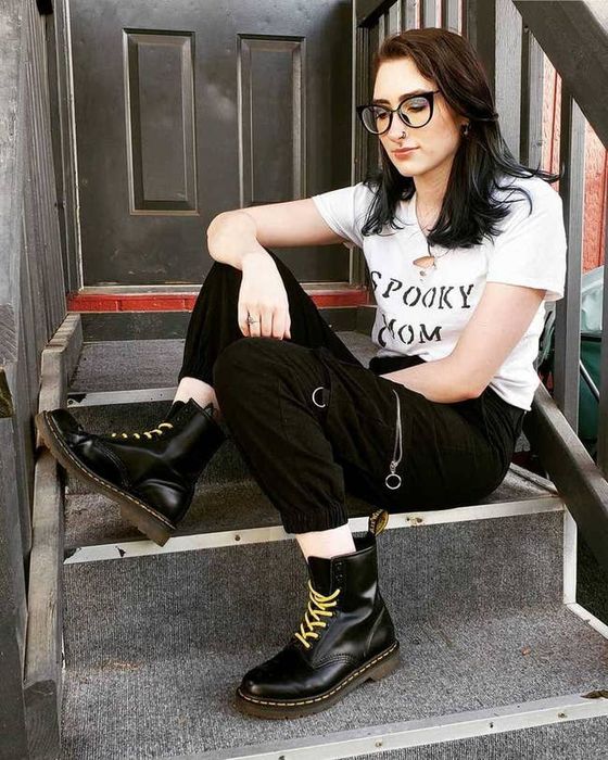 A model sitting on a stoop wearing black Dr. Martens boots.