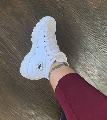 Reviewer wearing high-top white Converse sneakers with the iconic star logo, matched with burgundy trousers