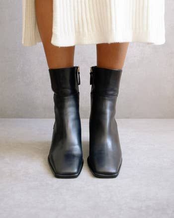 A front view of a model wearing black square-toe ankle boots.