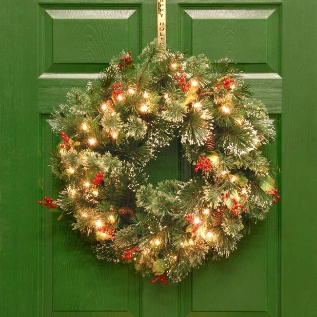 A festive holiday wreath with lights and red berries hanging on a door, adding a cheerful touch to the season’s decor