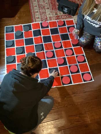 Two people engaged in a game of checkers on a large floor-sized checkerboard.