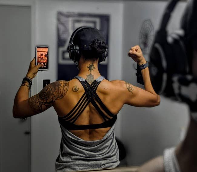A reviewer showcases the back of a gray tank top with an open back, revealing black crisscrossing bra straps.