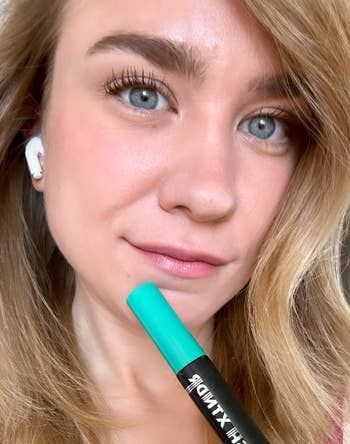 Close-up of a reviewer holding a mascara tube, showcasing fully done lashes.