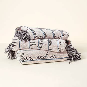 Three tasseled blankets stacked on top of each other, featuring handwritten lines of text