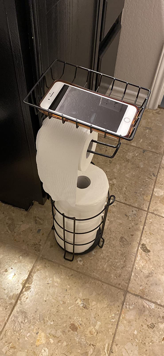 A review photo showcasing the toilet paper stand fully stocked with rolls, with a phone placed on the top shelf.