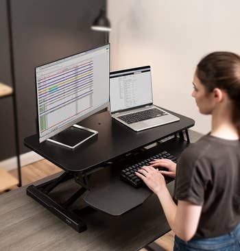 a model using a sit-to-stand desk converter in the standing position
