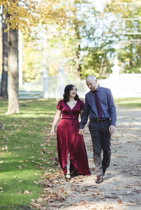 A writer is pictured with her fiancé, wearing a long burgundy satin wrap dress.