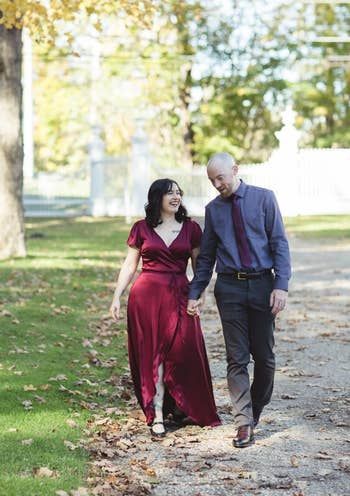 A writer is pictured with her fiancé, wearing a long burgundy satin wrap dress.