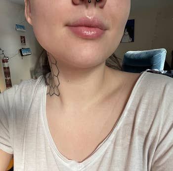 A reviewer with a geometric neck tattoo and a septum piercing, wearing a light-colored top in a cozy, well-lit room
