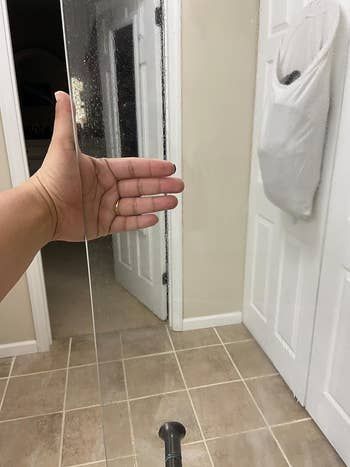 The same shower door with the reviewer’s hand, but now the door is completely spotless and clear