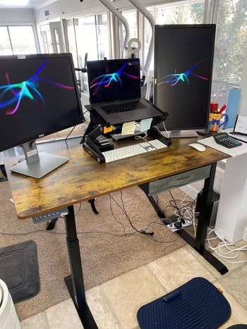 a reviewer’s workspace setup showcasing three monitors on an electric standing desk
