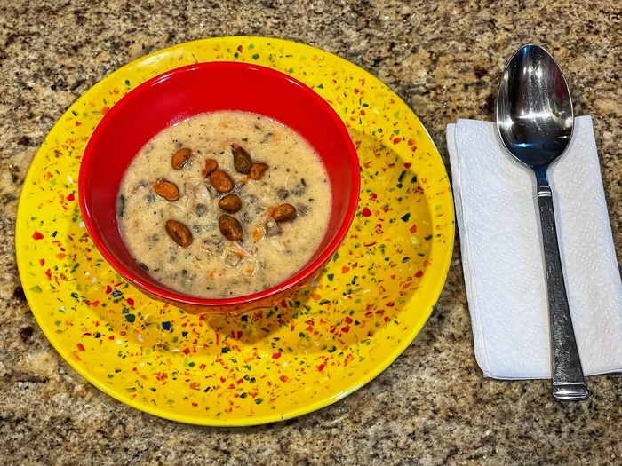 A bowl of creamy soup on a bright yellow speckled plate, accompanied by a neatly folded napkin and a spoon