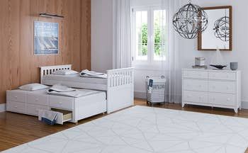 A white trundle bed with drawers placed in a bedroom.