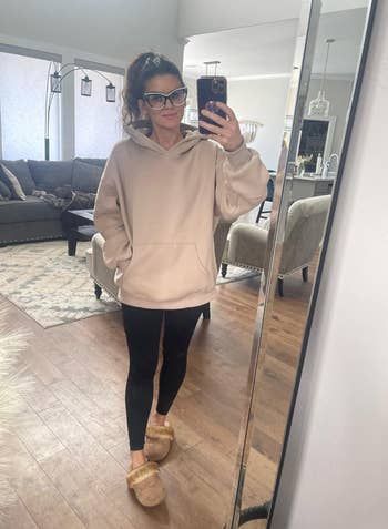 A reviewer sports an oversized cream-colored hoodie, embracing a comfortable and stylish vibe.