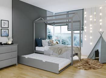 A stylish gray trundle canopy bed with the trundle extended for extra sleeping space.