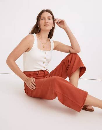 A model sitting on the floor, rocking rust-colored wide-leg jeans.