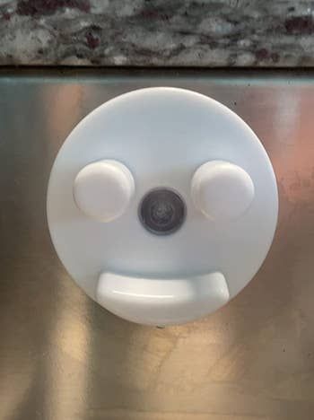 A white suctioned plastic piece with indents jutting out like a smiley face