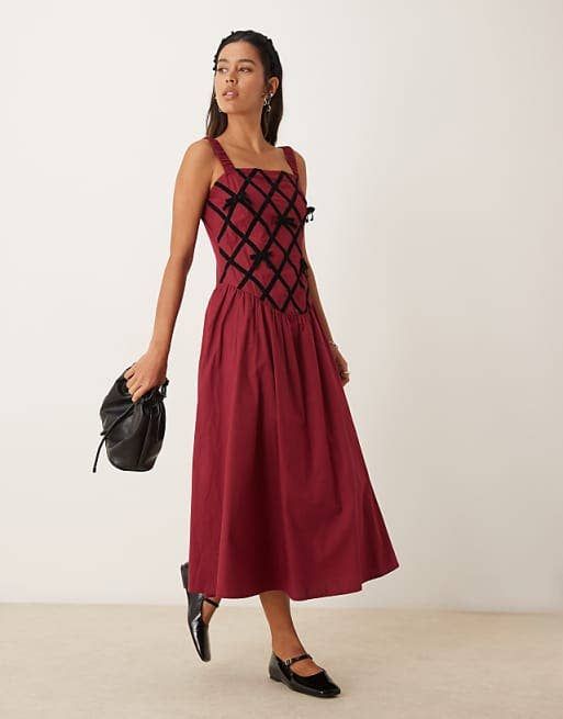 A model showcasing a chic, sleeveless dress with a bold geometric design, carrying a small handbag, posed for a shopping editorial