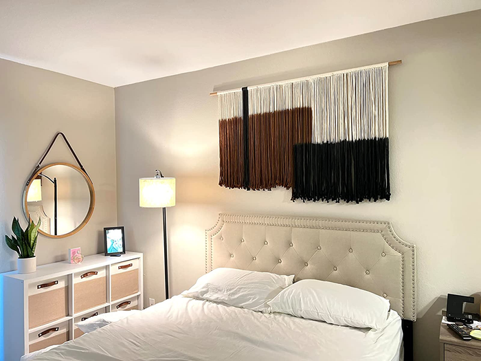 A reviewer’s photo of the black, brown, and white macrame wall hanging placed above their bed.
