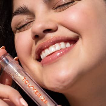 a model posing with the tube of lip gloss in the shade