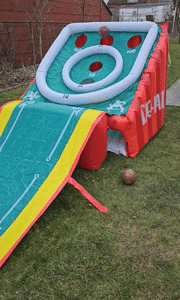 Inflatable skee-ball game set up on the lawn, with a ball rolling down the ramp