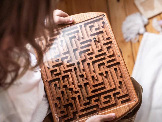 A child playing with a wooden maze, with a glass top to keep the ball inside.