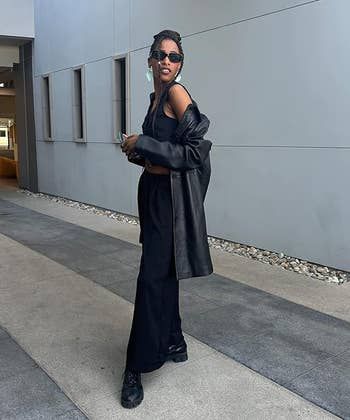 A reviewer in a chic outfit featuring a long coat, sunglasses, and wide-leg pants, walking through a modern urban setting. Perfect for a shopping feature