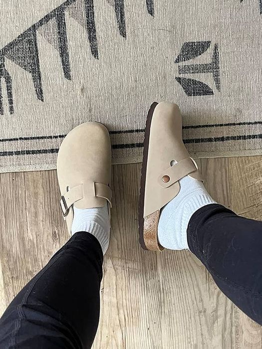 A reviewer displaying the top and side view of beige clogs.