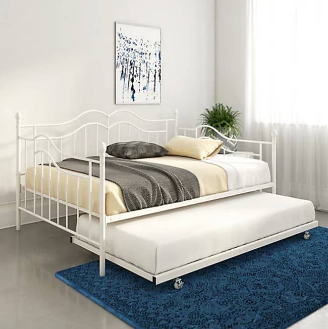 A lifestyle image showcasing a white metal bed with the trundle pulled out.